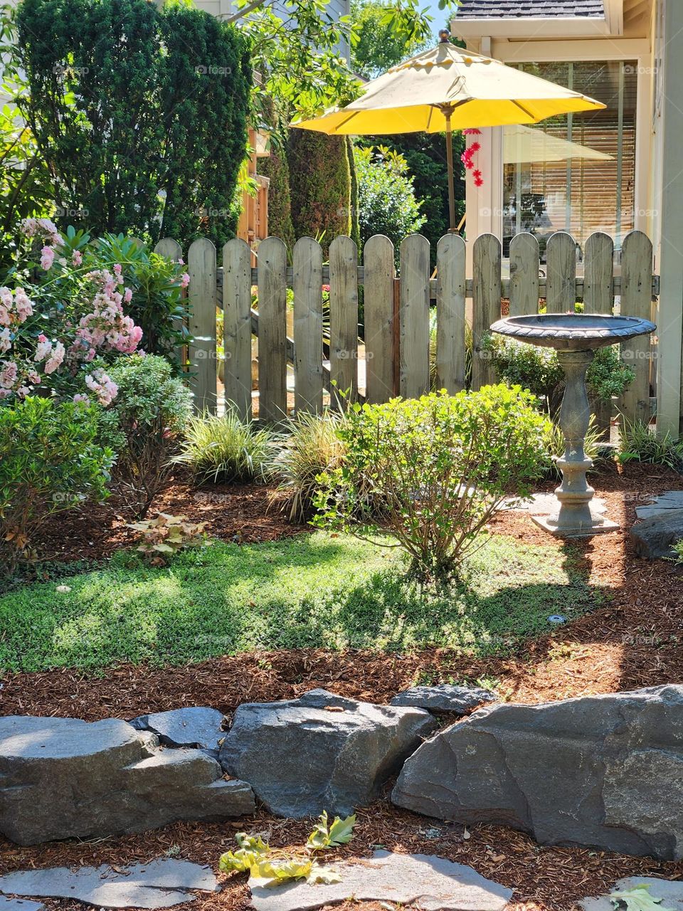 street view of a tranquil suburban home with garden, yellow umbrella and birdbath