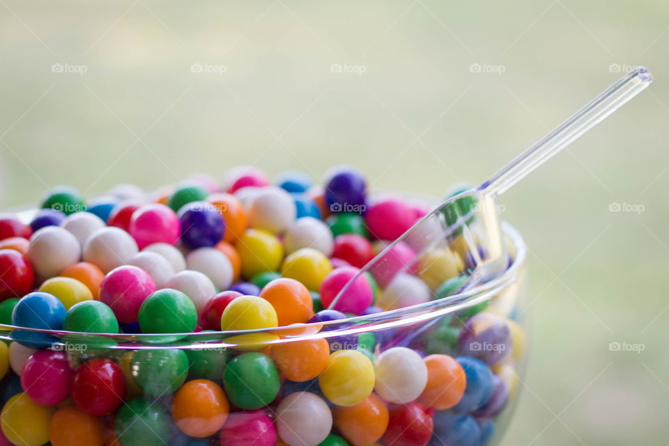 Colorful gum balls and candy in a clear container with a clear scoop 
