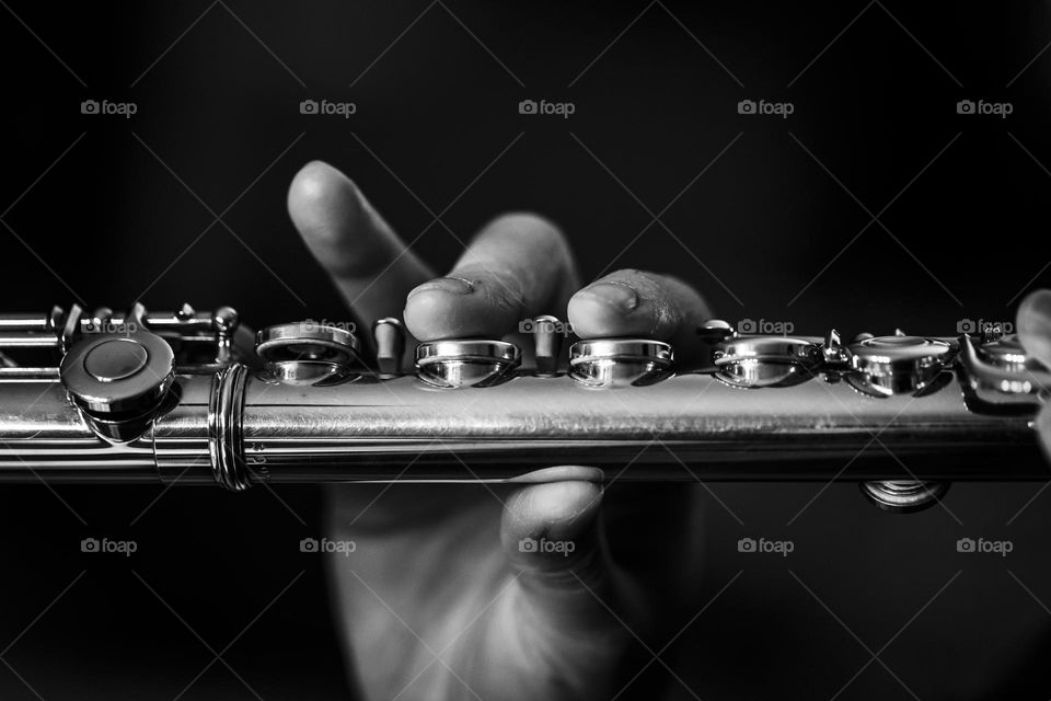 a black and white portrait of a hand with 2 fingers pressing the valves of a silver flute. the flutist is playing a song.