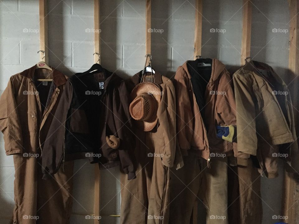 Still life of coveralls, jackets, hats and other cold weather gear hanging on hooks, ready for outdoor farm chores