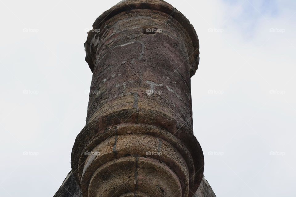 A part of a stone fort featuring a turret with a small window at the top against a cloudy sky