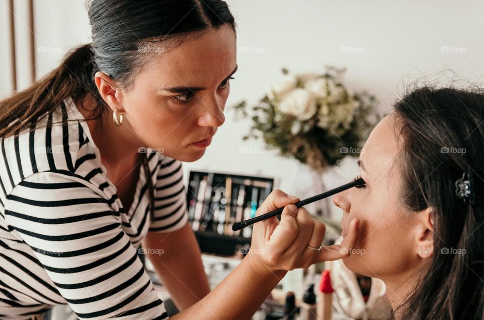 Beautician doing make-up on young woman in beauty salon