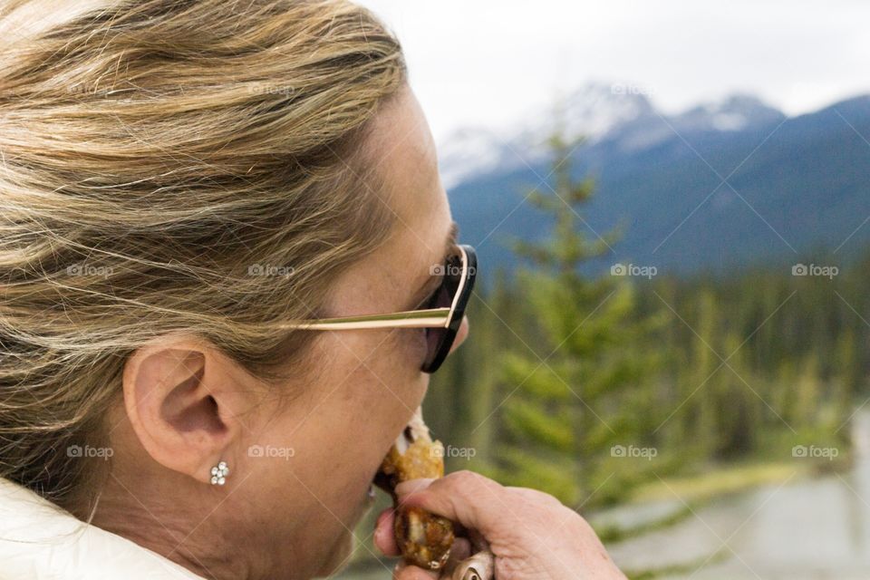 Woman with blonde hair eating while enjoying beautiful scenic view of Canada's Rocky Mountains near Banff Alberta 