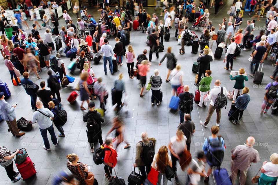 Looking down from above onto a crowded train station concourse at King's Cross in London, UK full of commuters, passengers and tourists waiting for information about their trains and platforms.