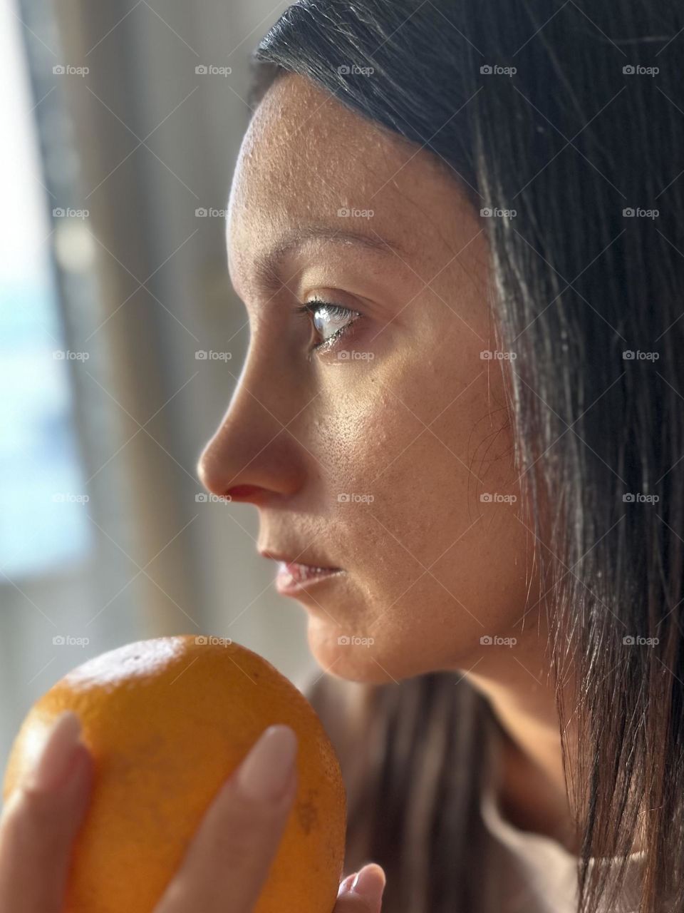 Later close up portrait of woman not wearing make up holding an orange 