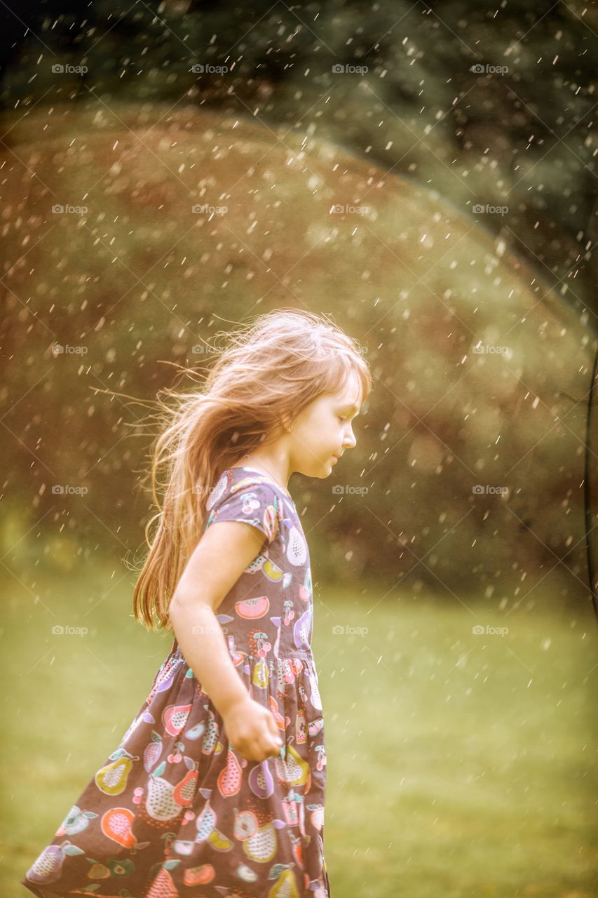Little girl running under rain in sunlight