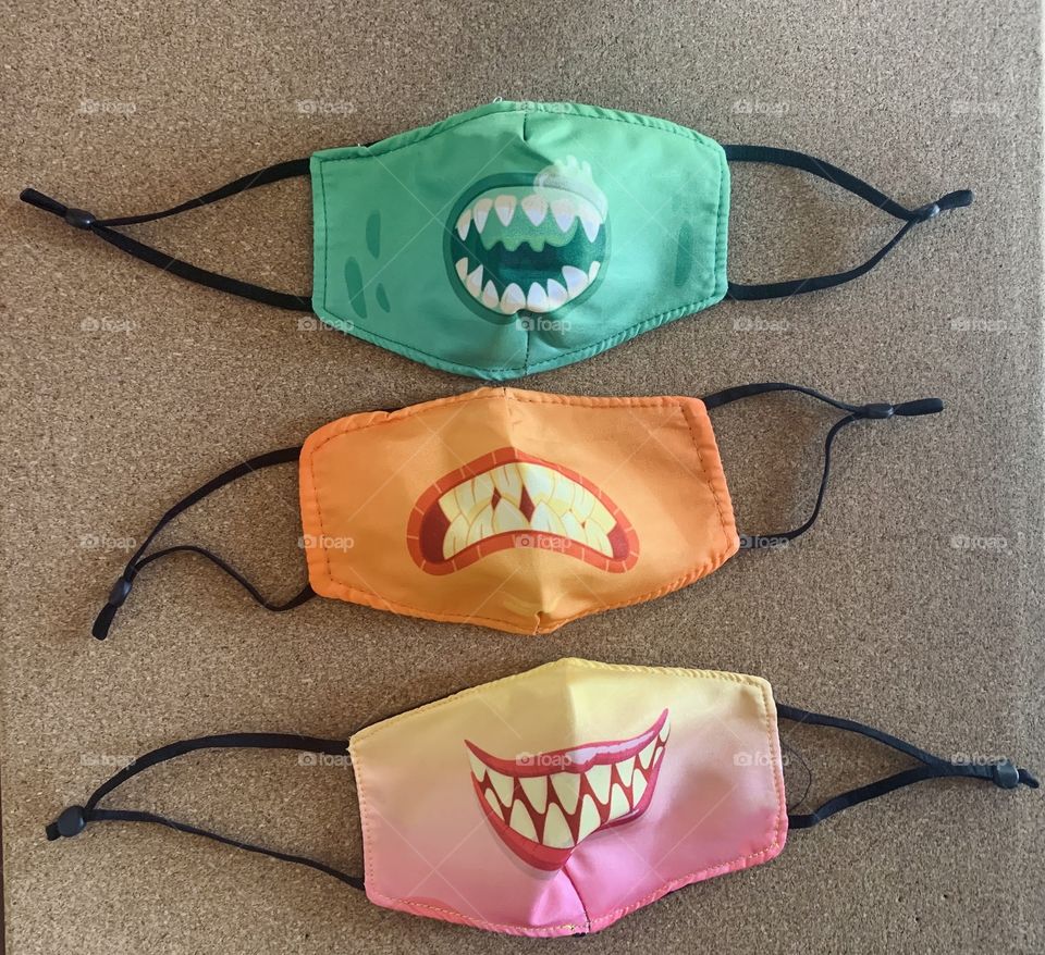 Three face masks of different colors and showing sharp vampire teeth 