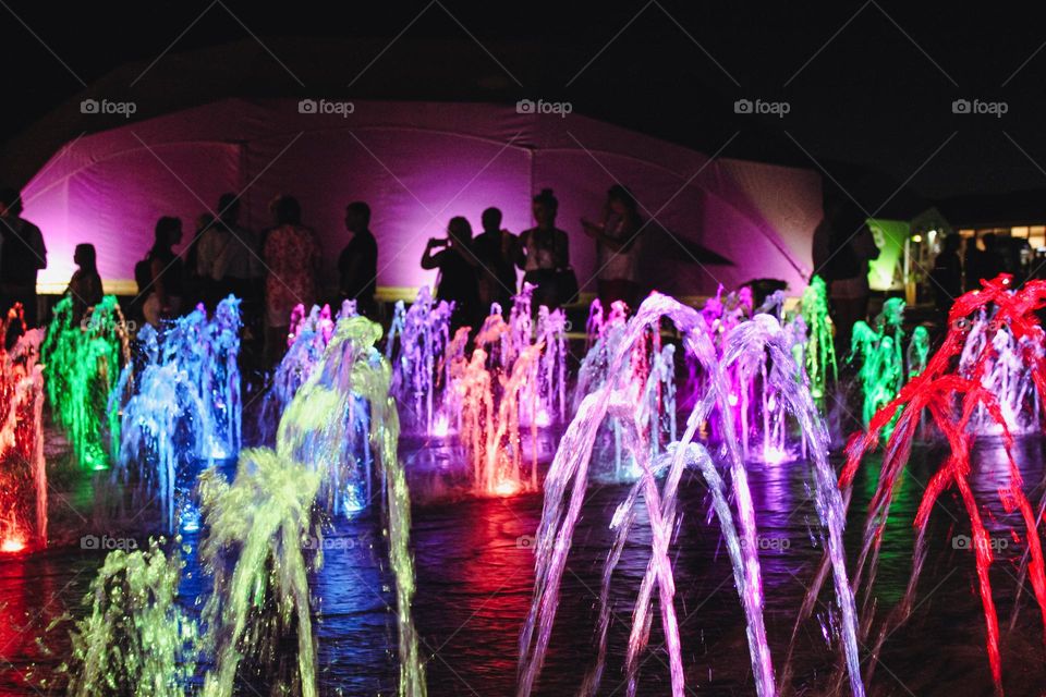 Party in the yard next to the backlight fountain. Multi -colored streams of water glowing night