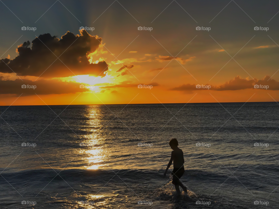 A young boy plays in a gorgeous ocean sunset .