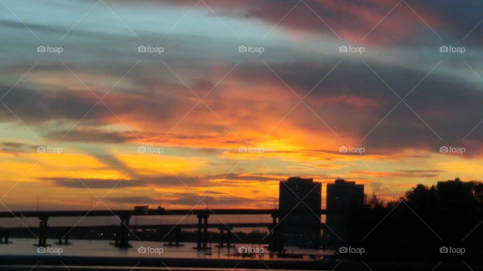Silhouette of bridges and buildings on the water with a sunset of blues, purples, oranges, pinks, and yellows.