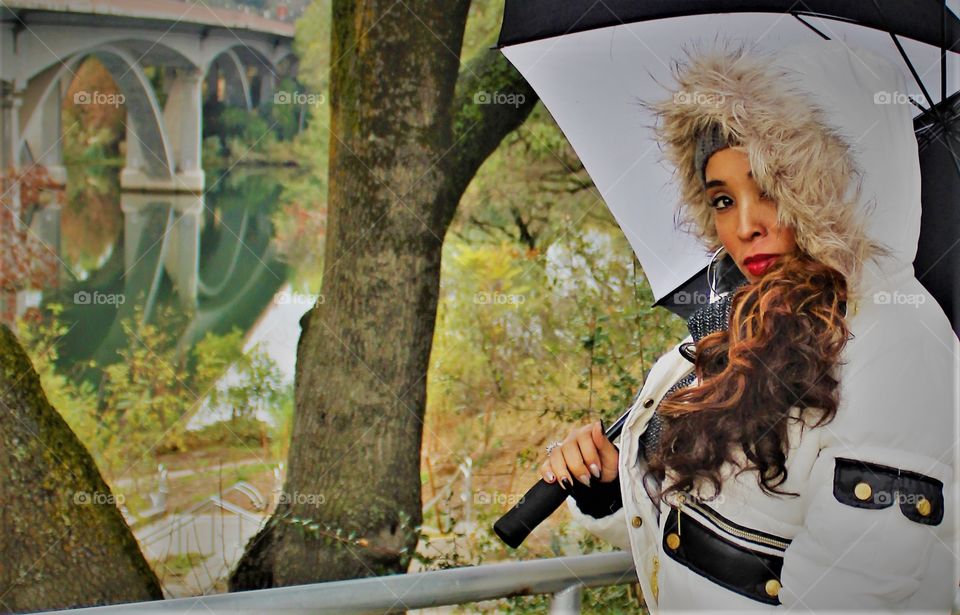 a woman holding a black and white umbrella with bridge in the background