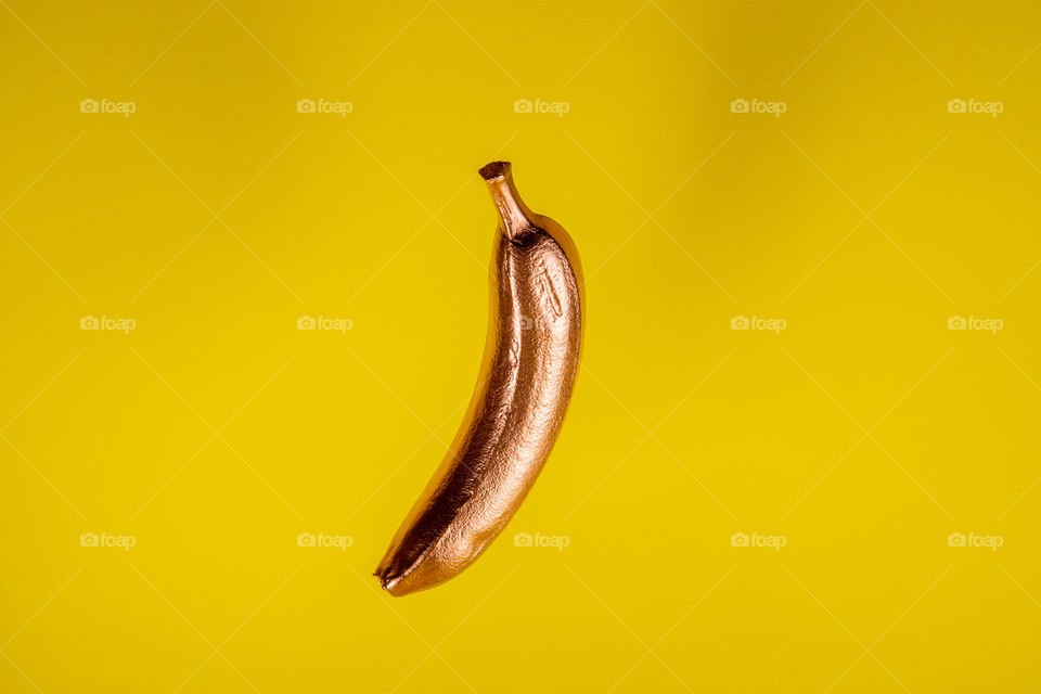 Floating gold banana on yellow background. Minimal food concept