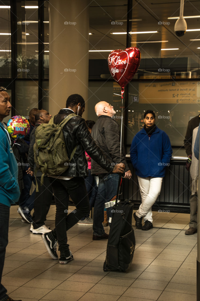 À man waiting for his love coming home, a heart shaped balloon strapped to his suitcase