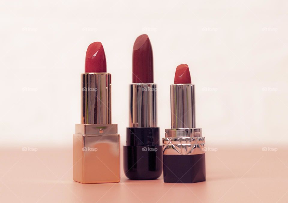 Three red lipsticks standing on a pink background with a blurred white brick wall,view from below. Concept female cosmetics, beauty salon.