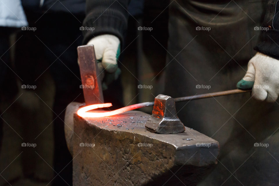 Blacksmith hand holding hammer with burning metal