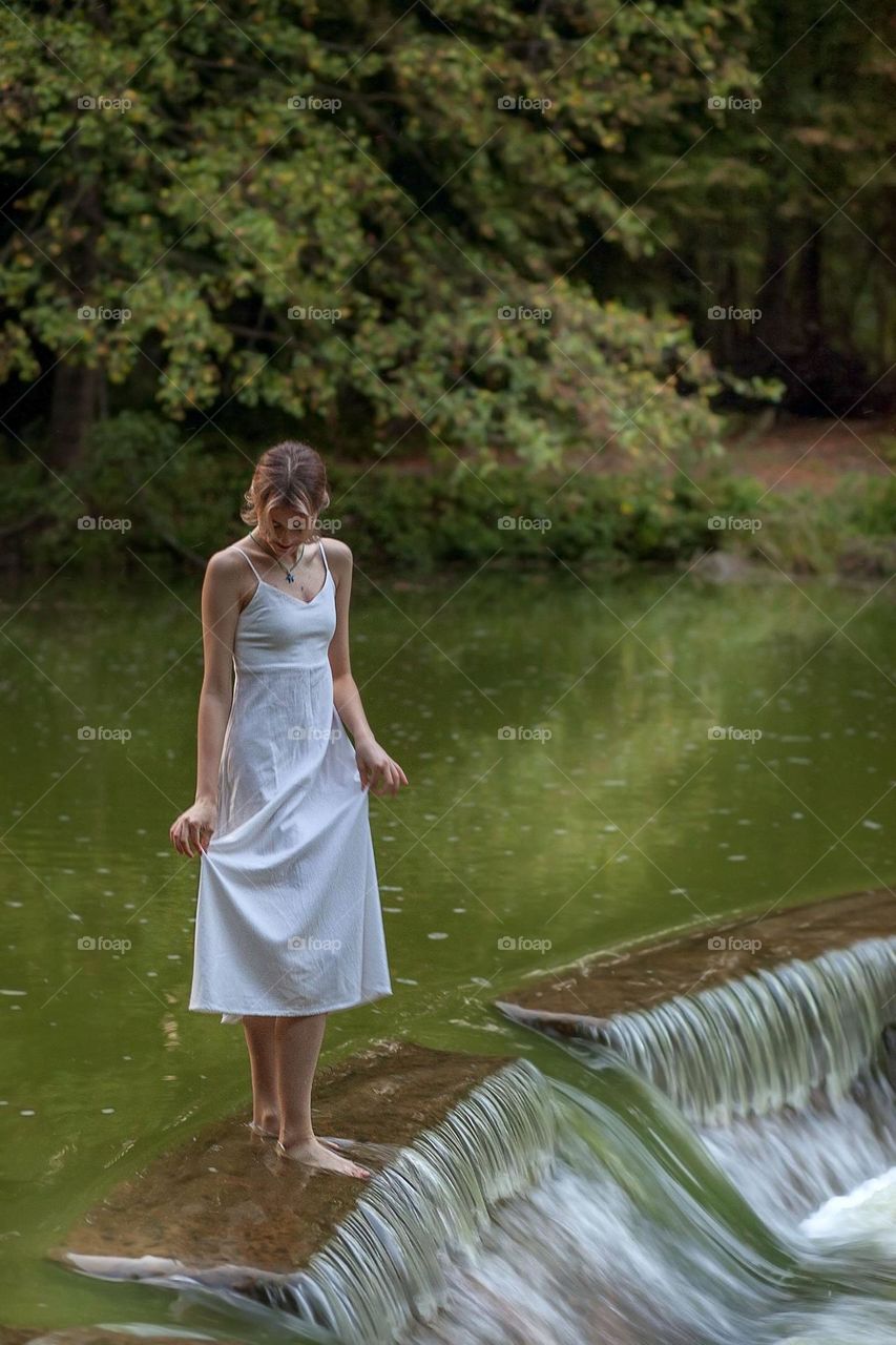 Teenage girl in a white dress near the water, waterfall.

￼

￼