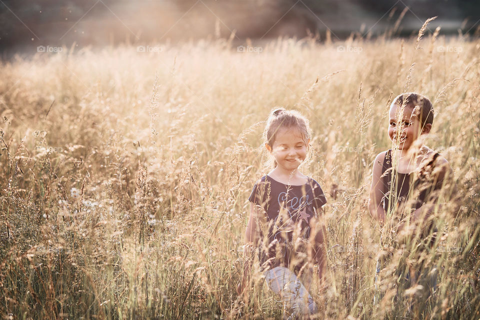 Little happy smiling kids playing in a tall grass in the countryside. Candid people, real moments, authentic situations