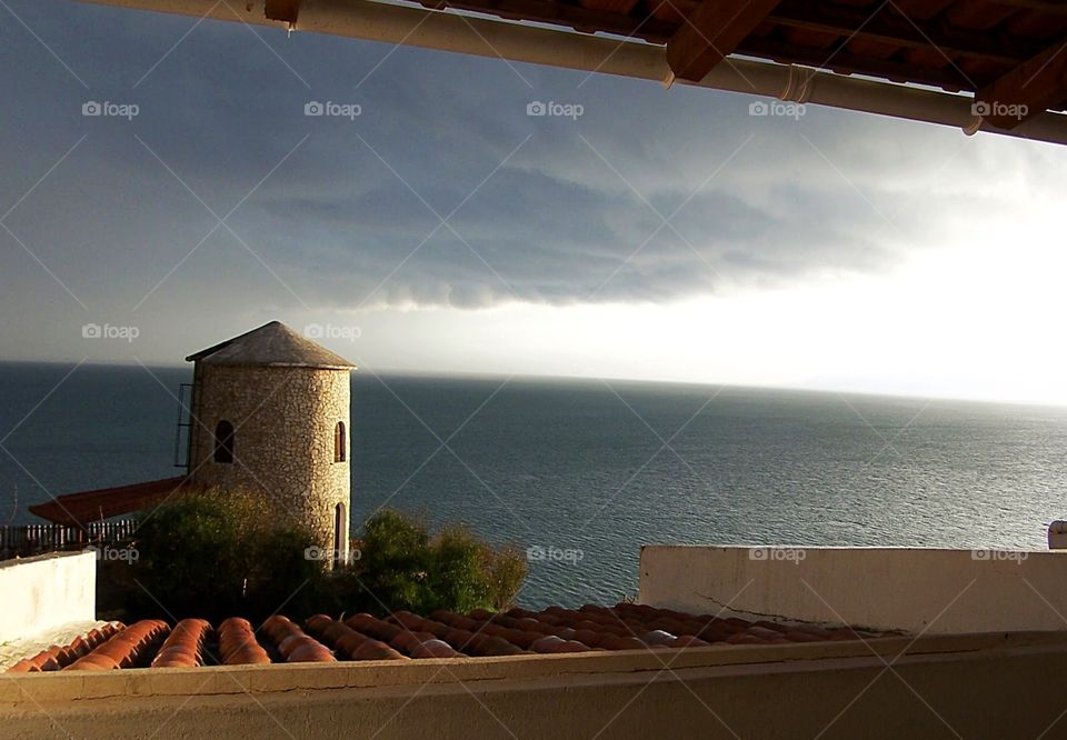 Window view  of an approaching storm and tower on the Aegean Sea on the Isle of Hydra in Greece