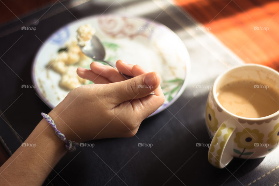 Hand of a young woman holding a spoon while she is eating a piece of cake in the breakfast 