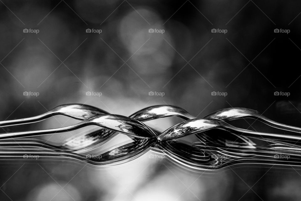 Black & white shot of overlapped spoons on a mirror outside in the sunlight provides the optical illusion of the spoons floating in the air & produces beautiful bokeh from the multiple reflective surfaces. 