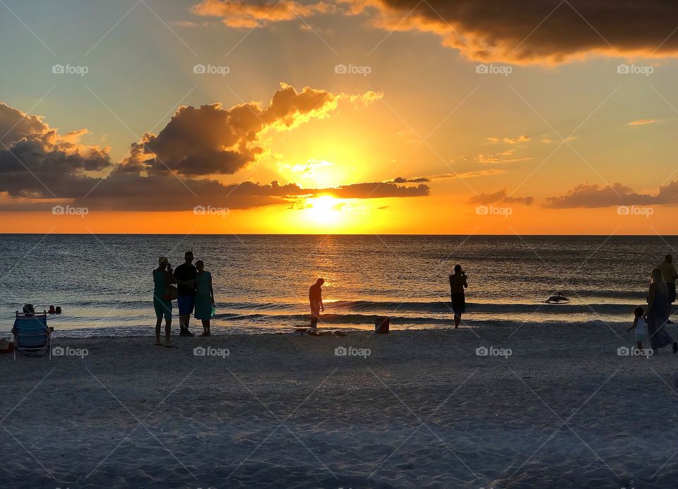 People gathered to watch a spectacular orange sunset over the ocean.