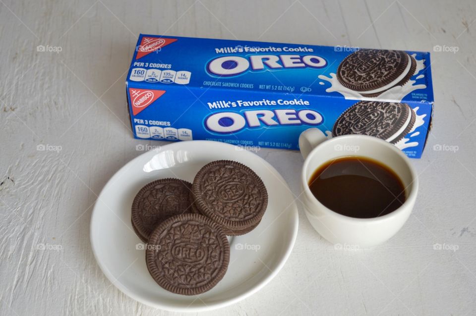 A flat lay of a pack of Oreos and Oreo cookies on a plate with a cup of coffee on a white background