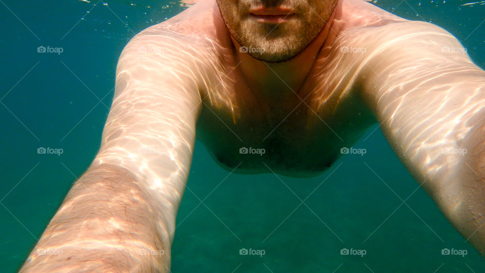 Man diving in the ocean, male underwater smiling,swimming and relaxing in big blue sea with his waterproof camera