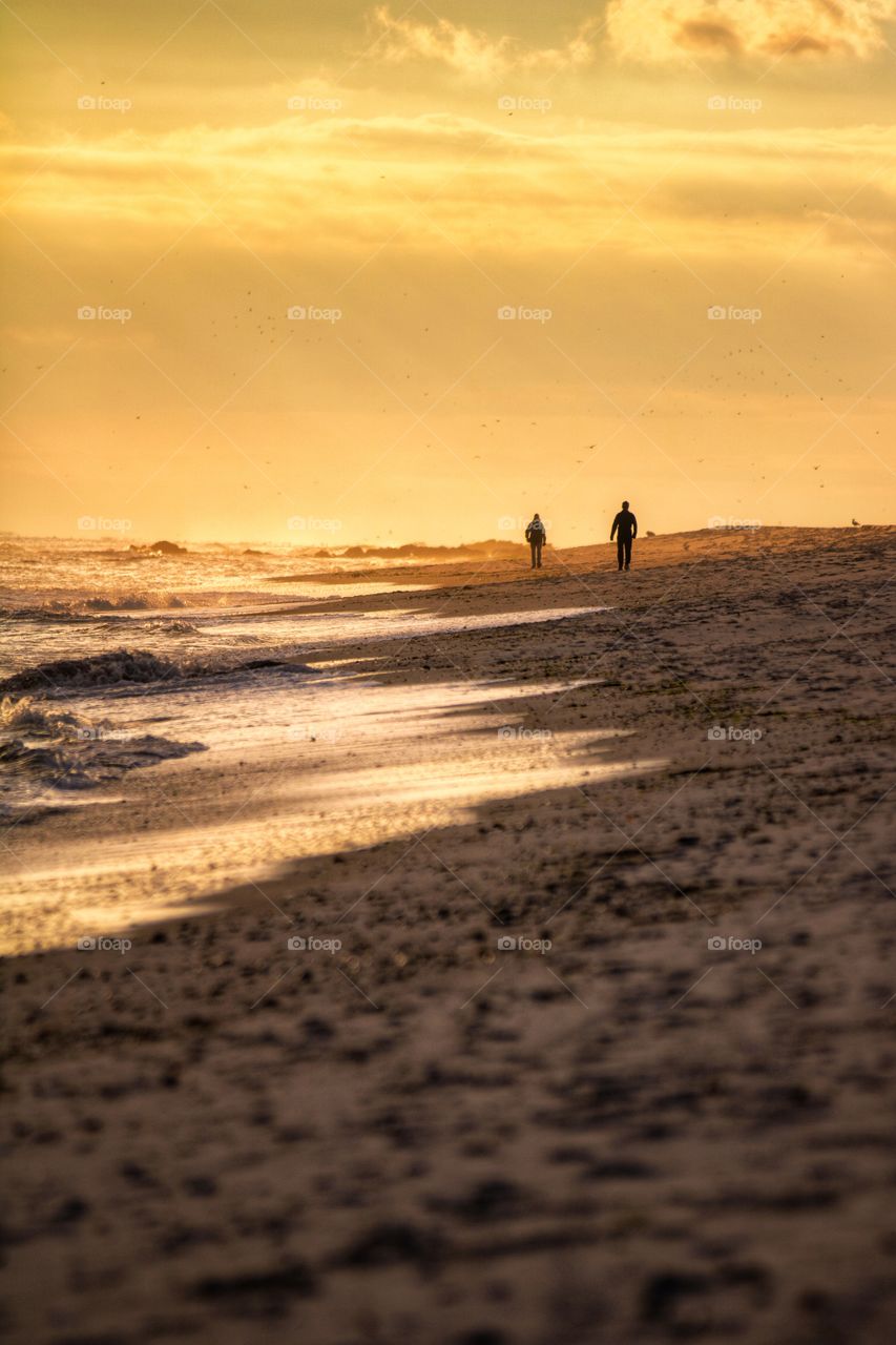 Silhouettes of people walking along a beautiful beach with golden sunset light shining down on the coast