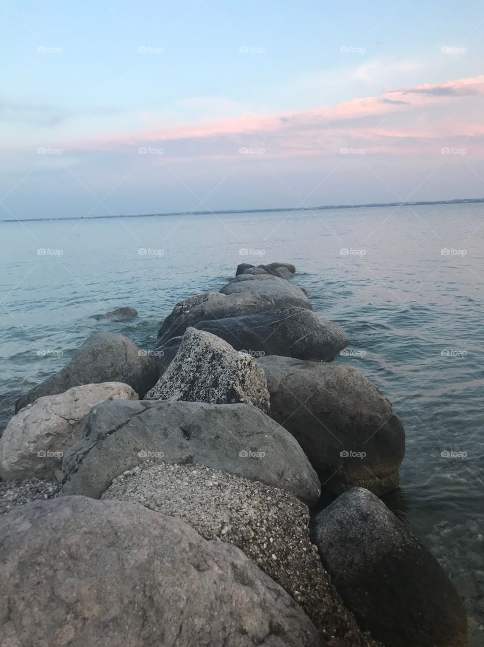 Big rocks form a straight line to the lake, the water is clear and very cool . sunset, the light blue sky appeared pink clouds . The colors reflected on the water looks so romantic