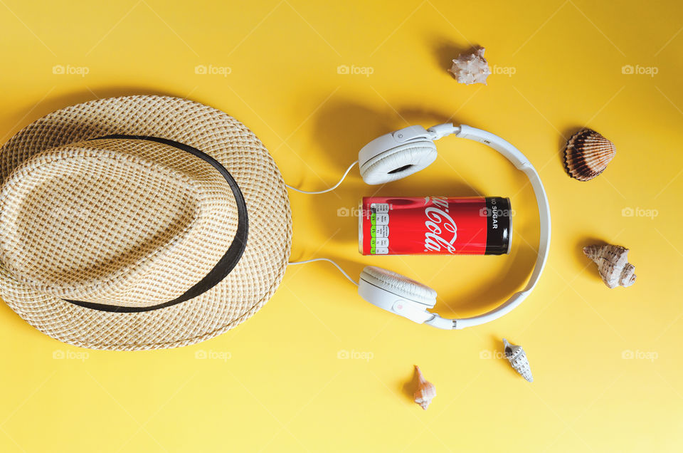 Travel under Covid-19 and new normal concept. Top view of medical face mask, can of Coca-Cola, phone and beach hat on yellow background. Creative ideas of prevent Coronavirus