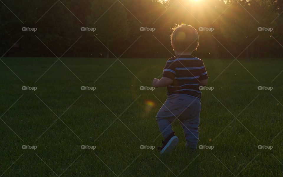 Minimal photo with child walking in field of grass at dusk