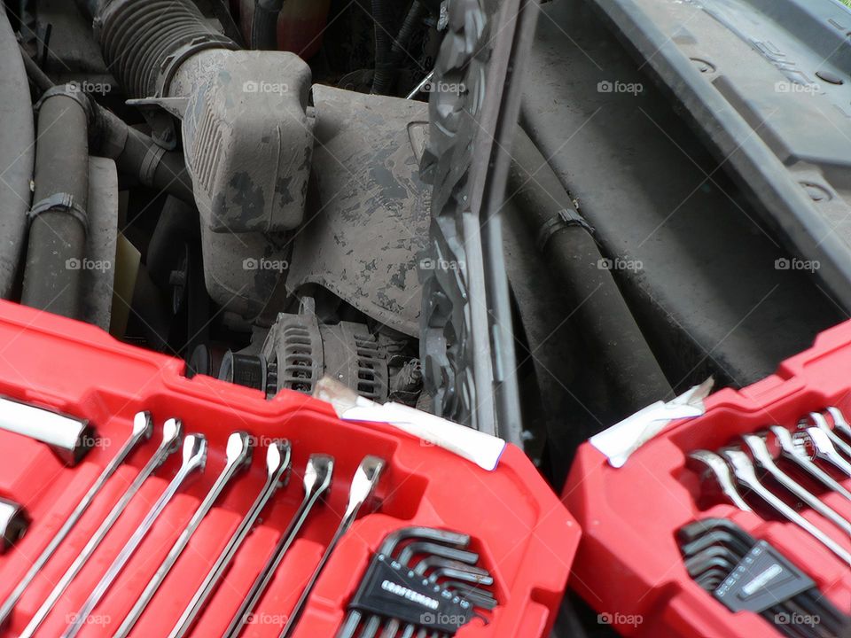 Under the hood of a red pickup truck with combination wrench set tools organized in a red tool hard case by the work station with its reflection from a mirror.