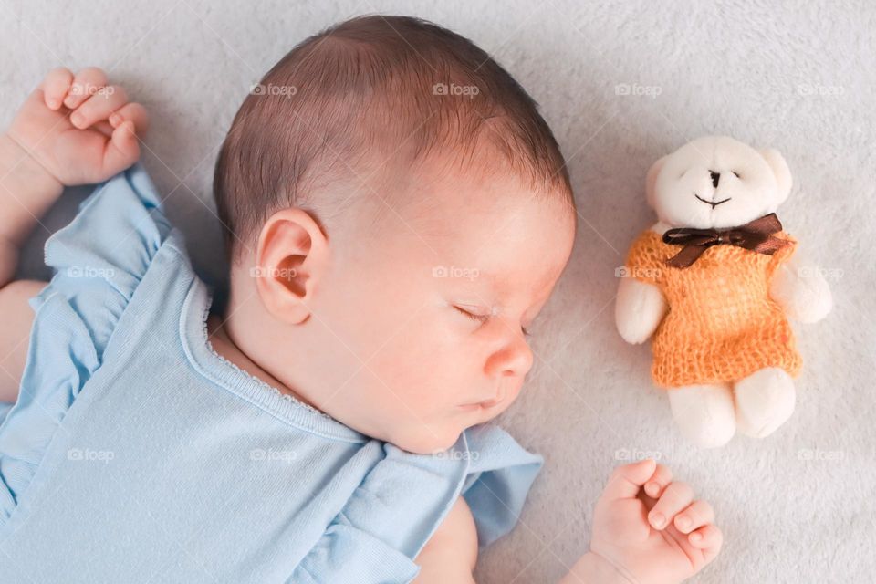 One beautiful caucasian sleeping baby with a teddy bear toy on the bed,close-up top view. The concept of sleeping children.