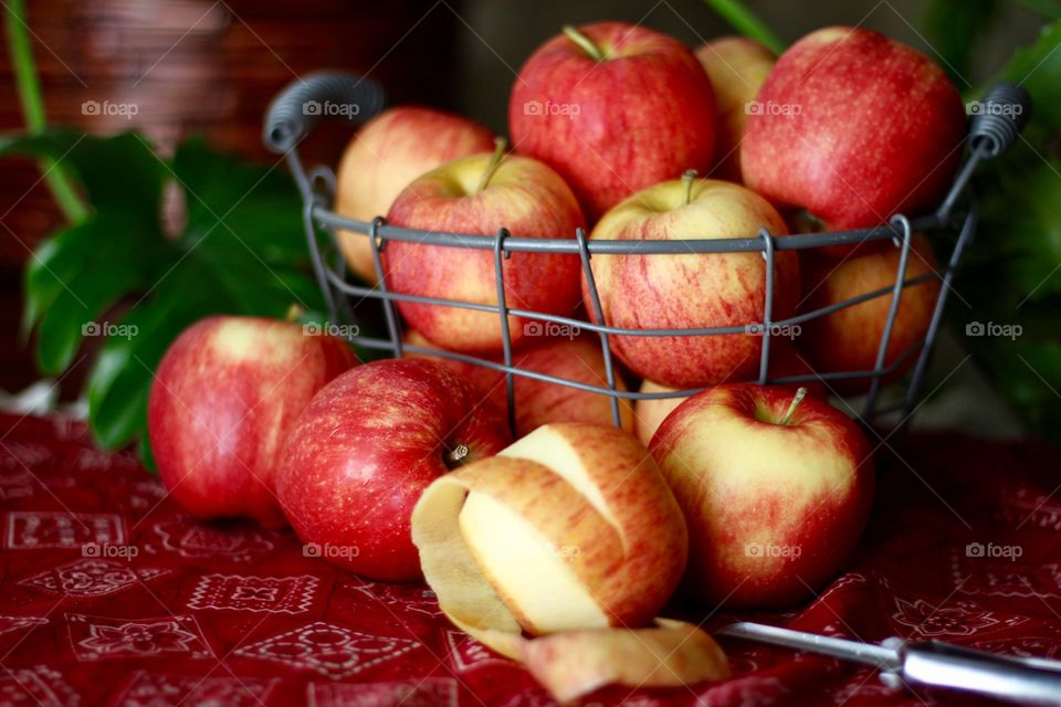 Fruits - Gala apples in a wire basket with a partially peeled apple and peeler on a red bandana-print tablecloth