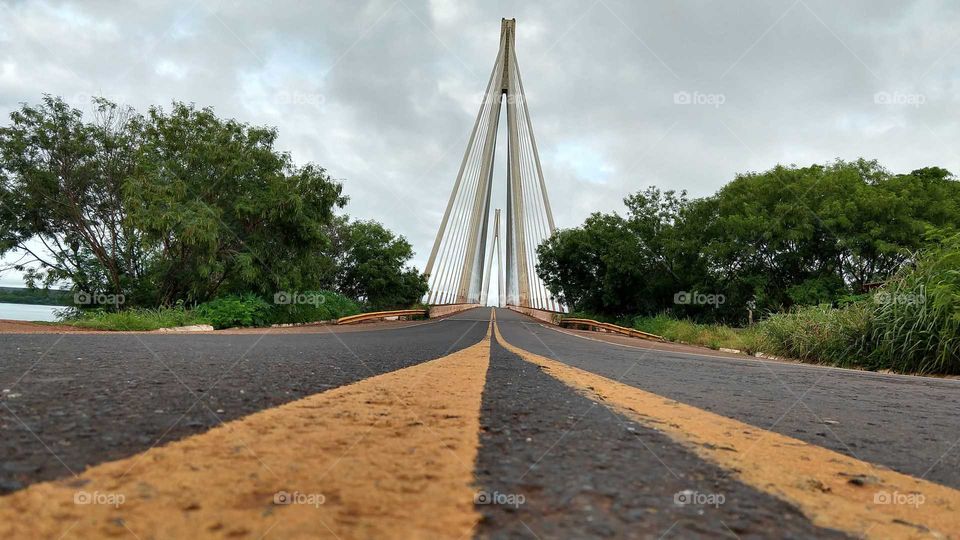 Faixa amarela do asfalto e ponte suspensa.