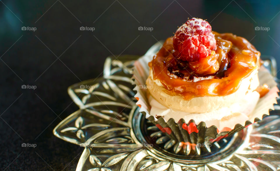 Beautiful decadent dessert cupcake with melted caramel nest and fresh raspberry on buttercream frosting on table 