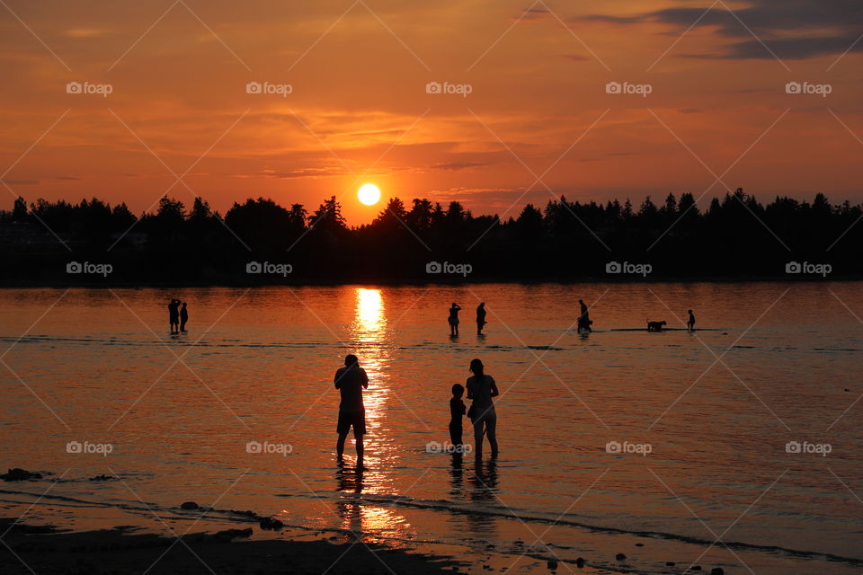 People in shallow water watching the beautiful sunset over the ocean 