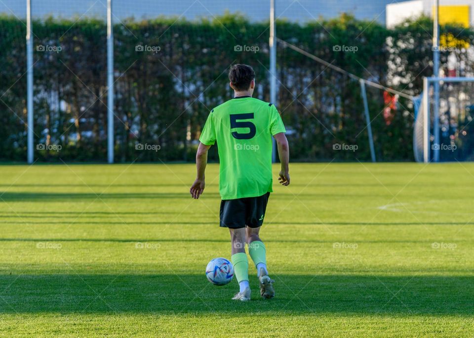 Rear view of football player running with a ball at an official match