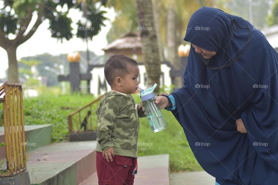 A mother provides drinking water for her 1.5 year old child.  Photo taken in the Beautiful Indonesia Miniature Park Area, Jakarta, on Sunday 19 March 2023