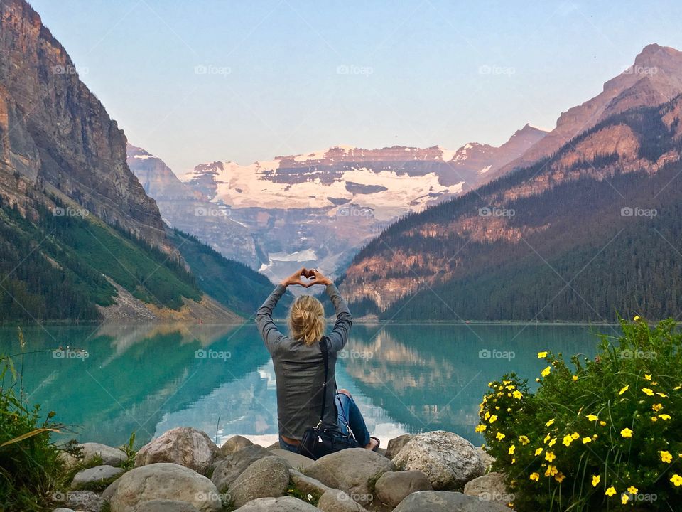 Lake Louise near Banff Alberta
Woman sitting in front of scenic glacial mountain lake making heart sign with hands 