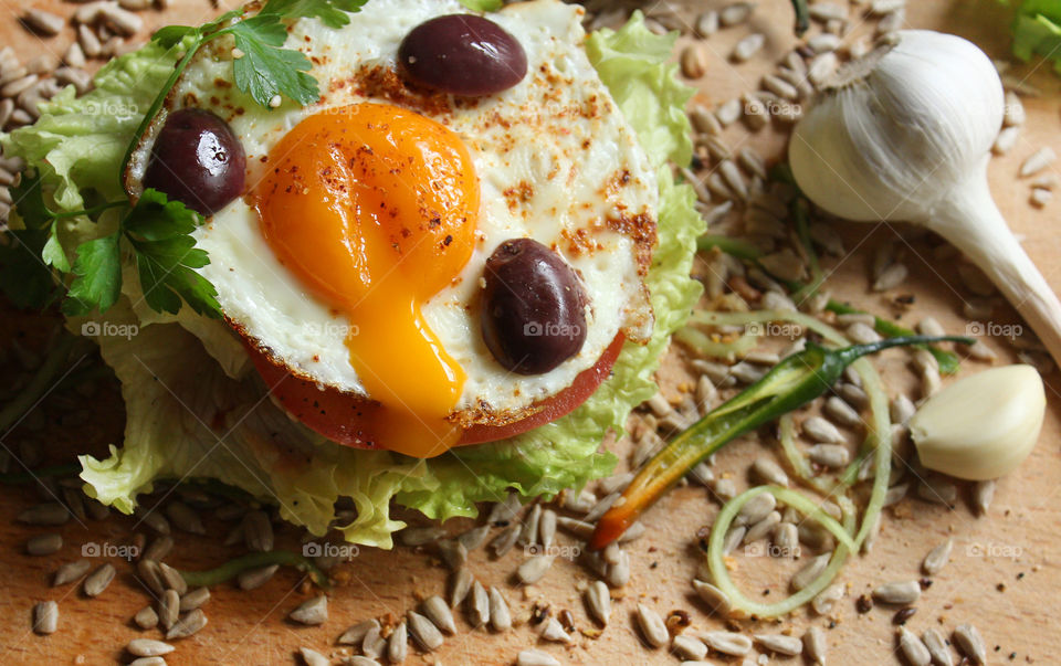 Tasty burger with fried egg, olives, lettuce, seeds, yolk, garlic, hot pepper