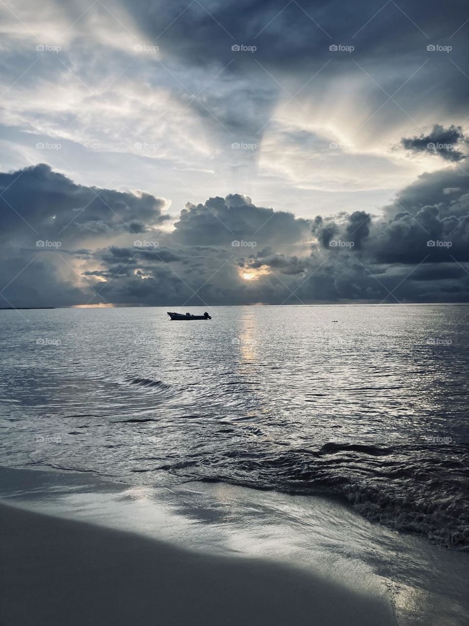 mysterious deep ocean during sunrise in méxico, rain season, storm clouds are on the sky, sun is peaking throughout them, boat is being slowly moved by waves 