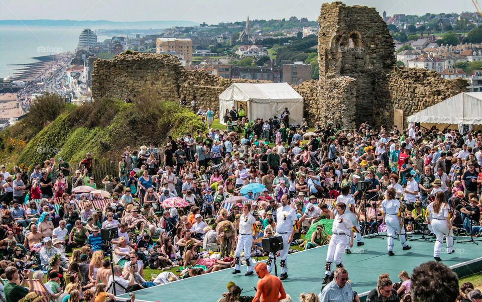 Morris dancers perform on stage to a large audience in the walls of the castle, at Hastings Traditional Jack in the Green. The view stretches out along the Sussex coastline - U.K. 2008