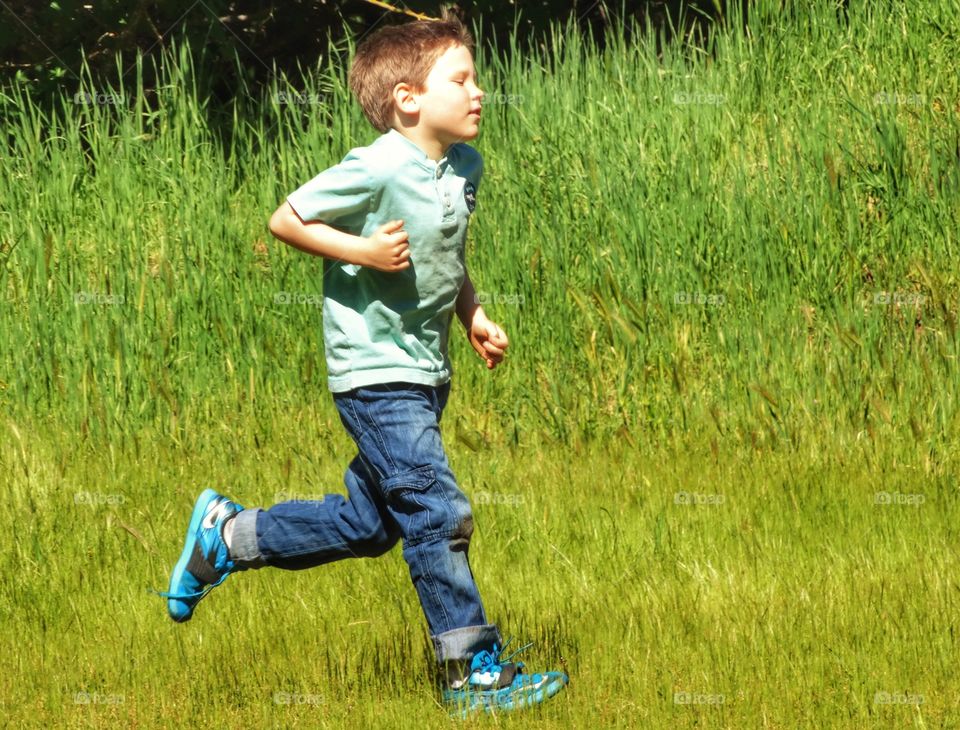 Love Running. Young Boy Running Across A Green Field
