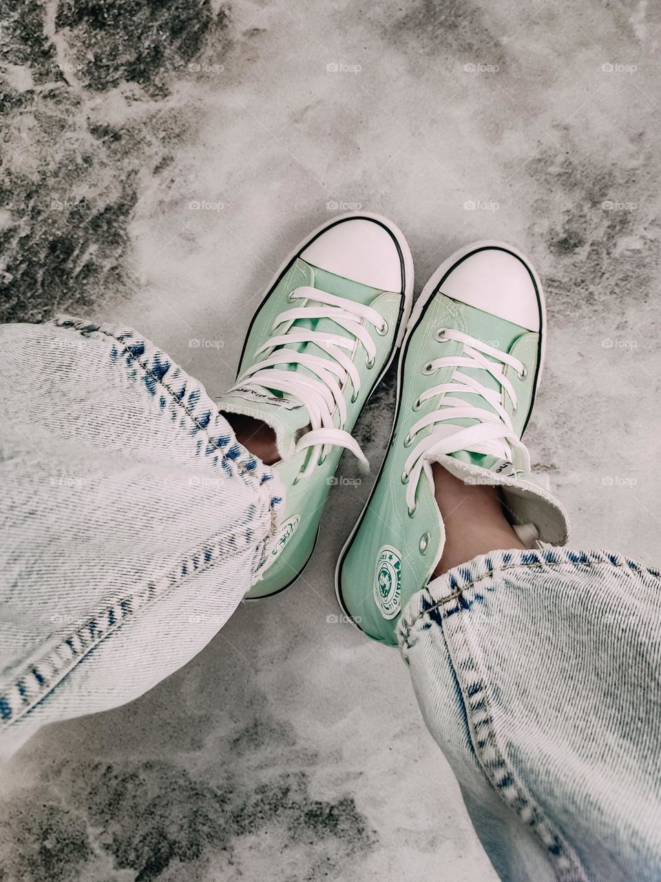 Mint green converse sneakers on the gray marble background. Woman's legs in sneakers and light blue jeans. Youth style fashion