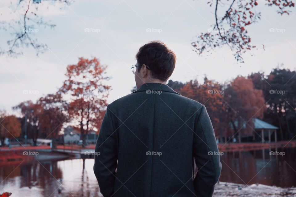 A young man standing with his back on a bridge against the background of a lake