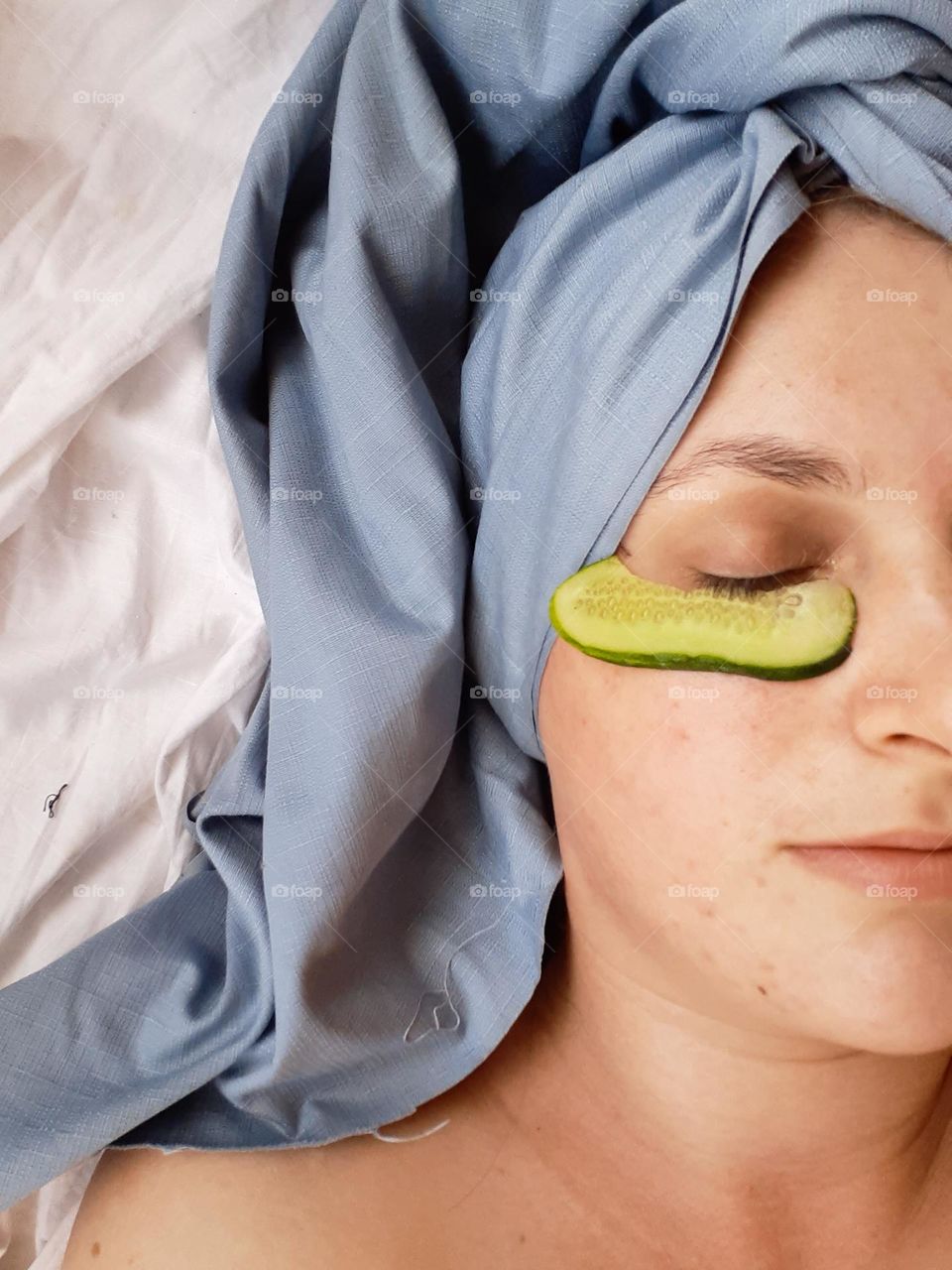 A pale female face during home cosmetic procedures, namely a cucumber mask