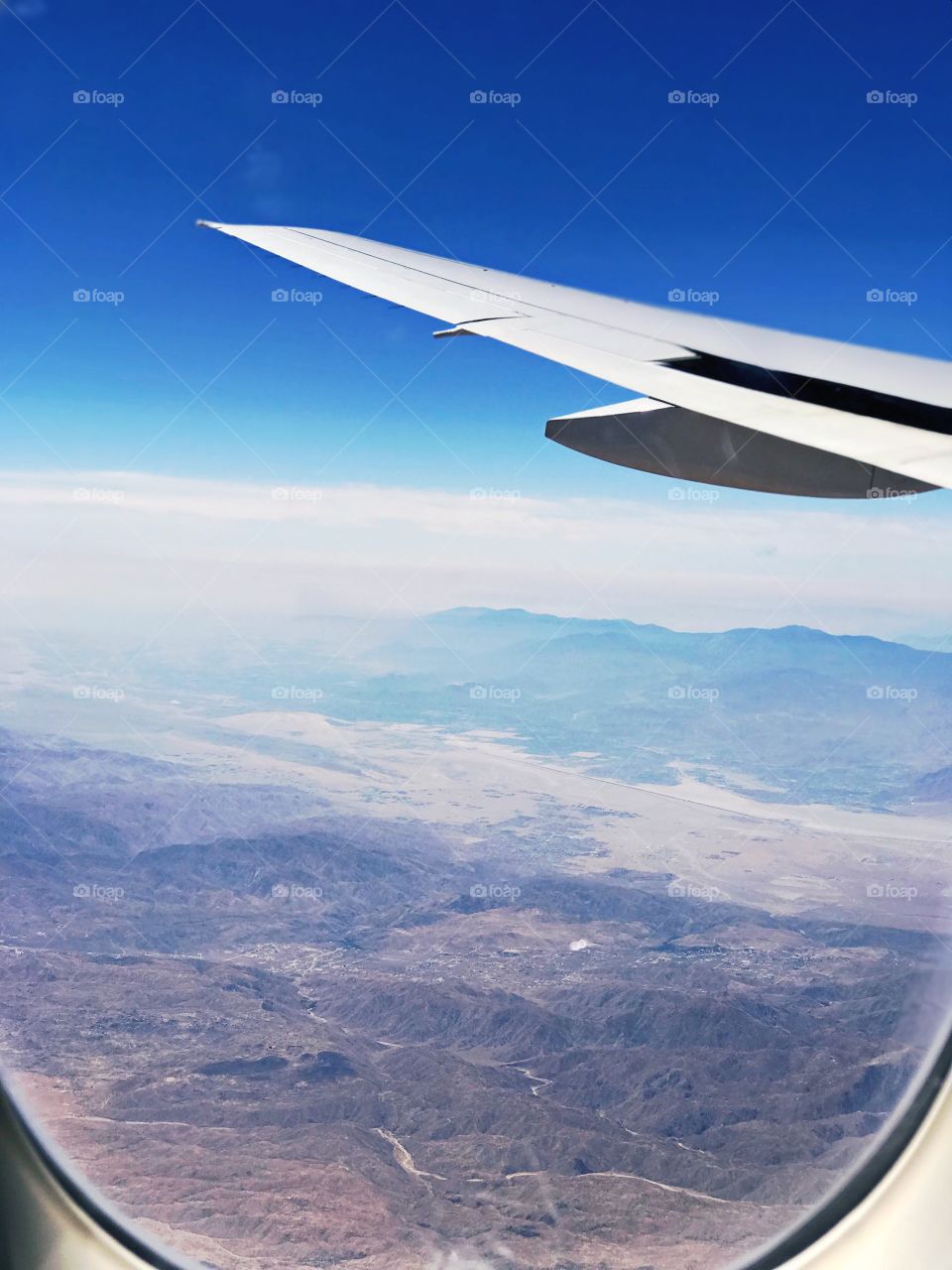 Flying United from Newark, New Jersey to Denver, Colorado; A view out the window with the airplane wing. Bright, Deep Blue sky, clouds, and mountain/hills