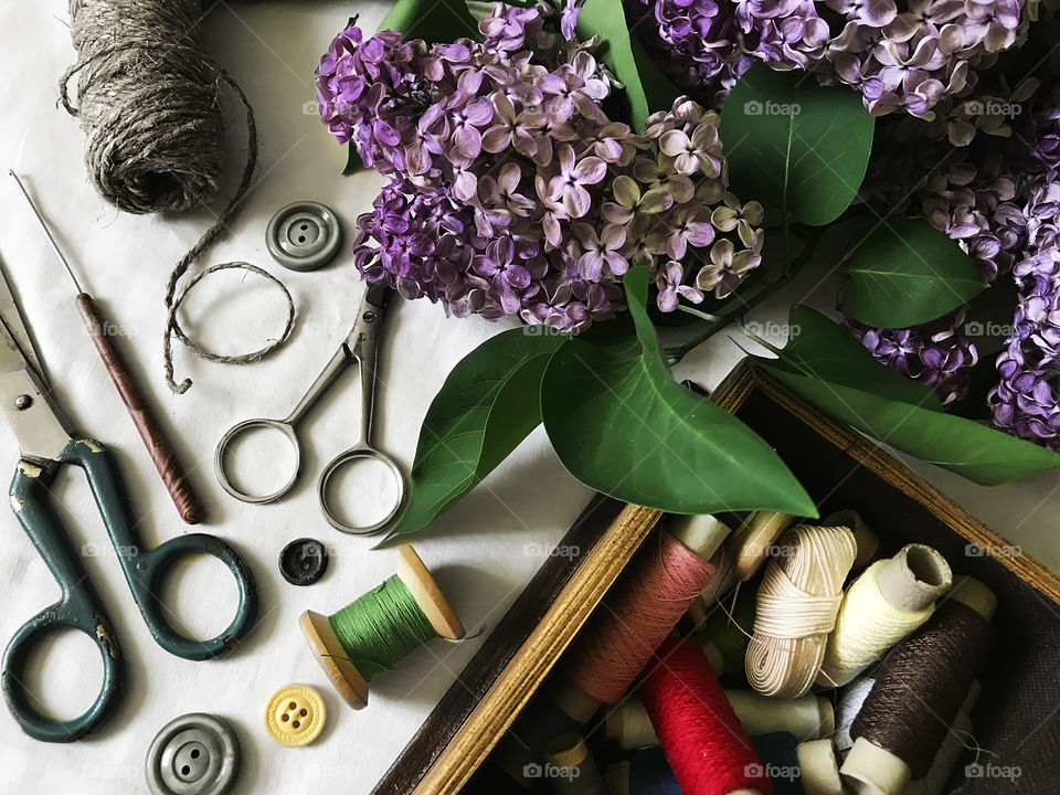 Flat lay sewing items - threads, scissors, buttons - sewing kit decorated by lilac flowers 