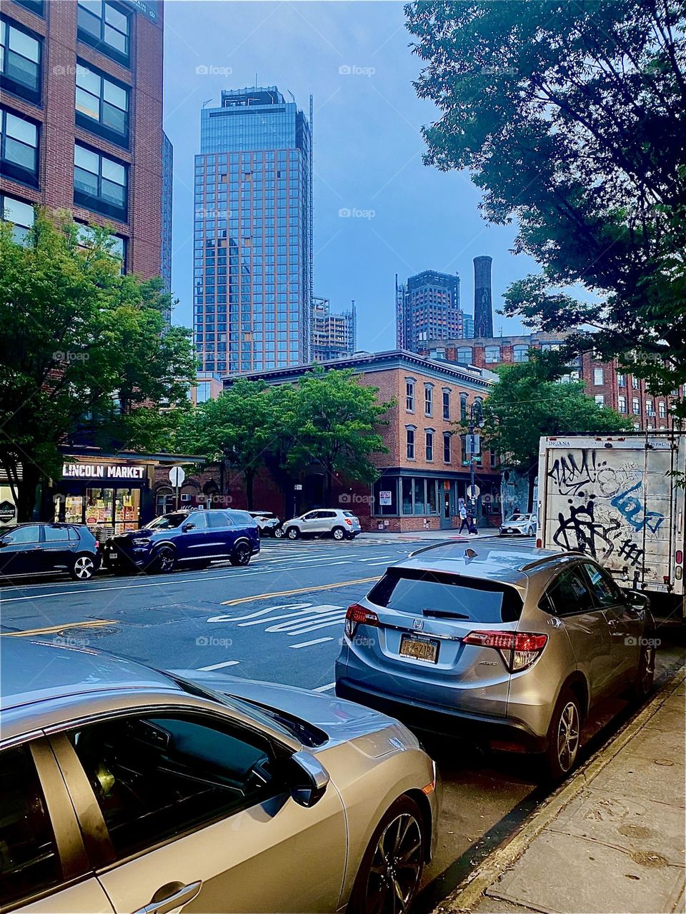 The streetlights are beginning to be illuminated for the evening, parking cars have their lights on here at “Manhattan Ave” and “Clay St” in “Greenpoint”, Bklyn by the “Pulaski Bridge” at “Newtown Creek”. 2023. Hypnotic Productions